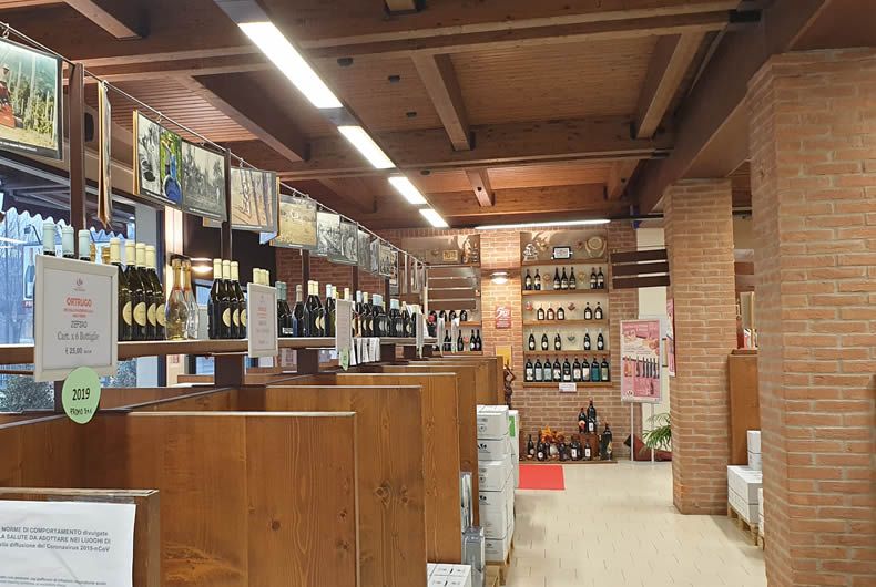 Interno enoteca Val Tidone: scaffali di legno con bottiglie di vino, foto appese e parete in mattoni.