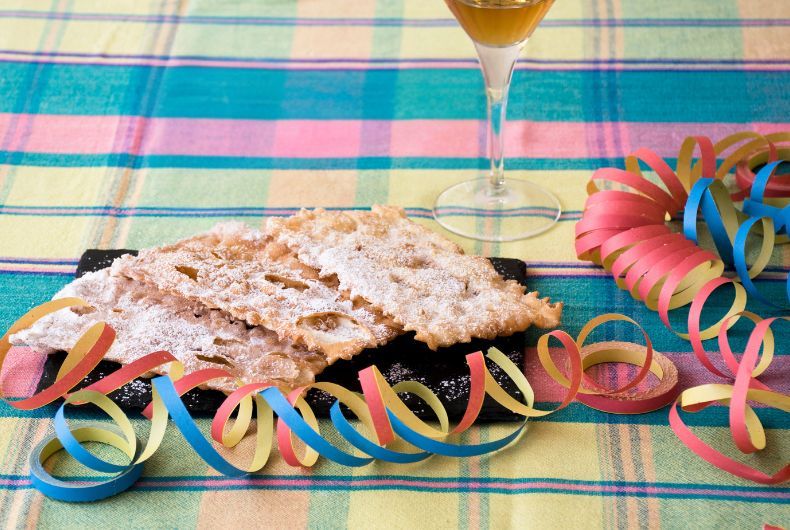 Dolci di Carnevale piacentini, chiacchiere fritte con zucchero a velo e vino dolce, sfondo a quadri e festoni colorati.