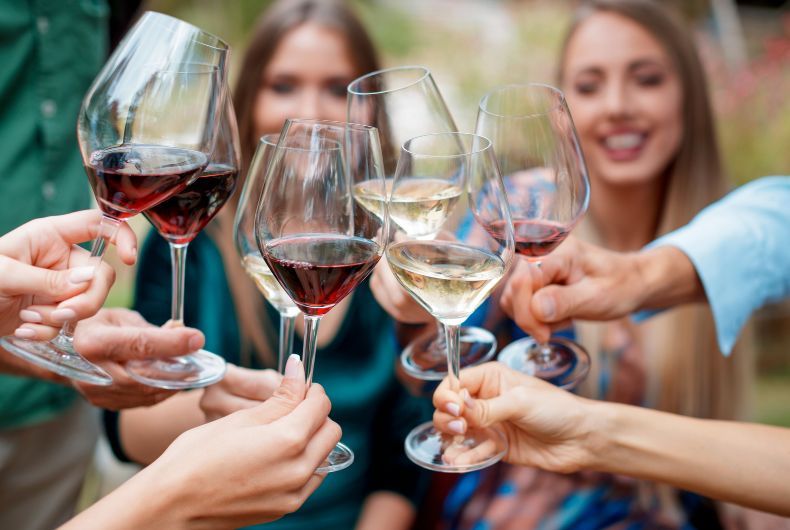 Brindisi con vino da tavola: calici di vino rosso e bianco sollevati da persone sorridenti. Celebrazione con vini Valtidone.