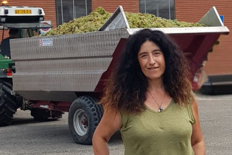 Sara Monaco sorride davanti a un rimorchio agricolo carico di uva appena raccolta presso la Cantina Valtidone.